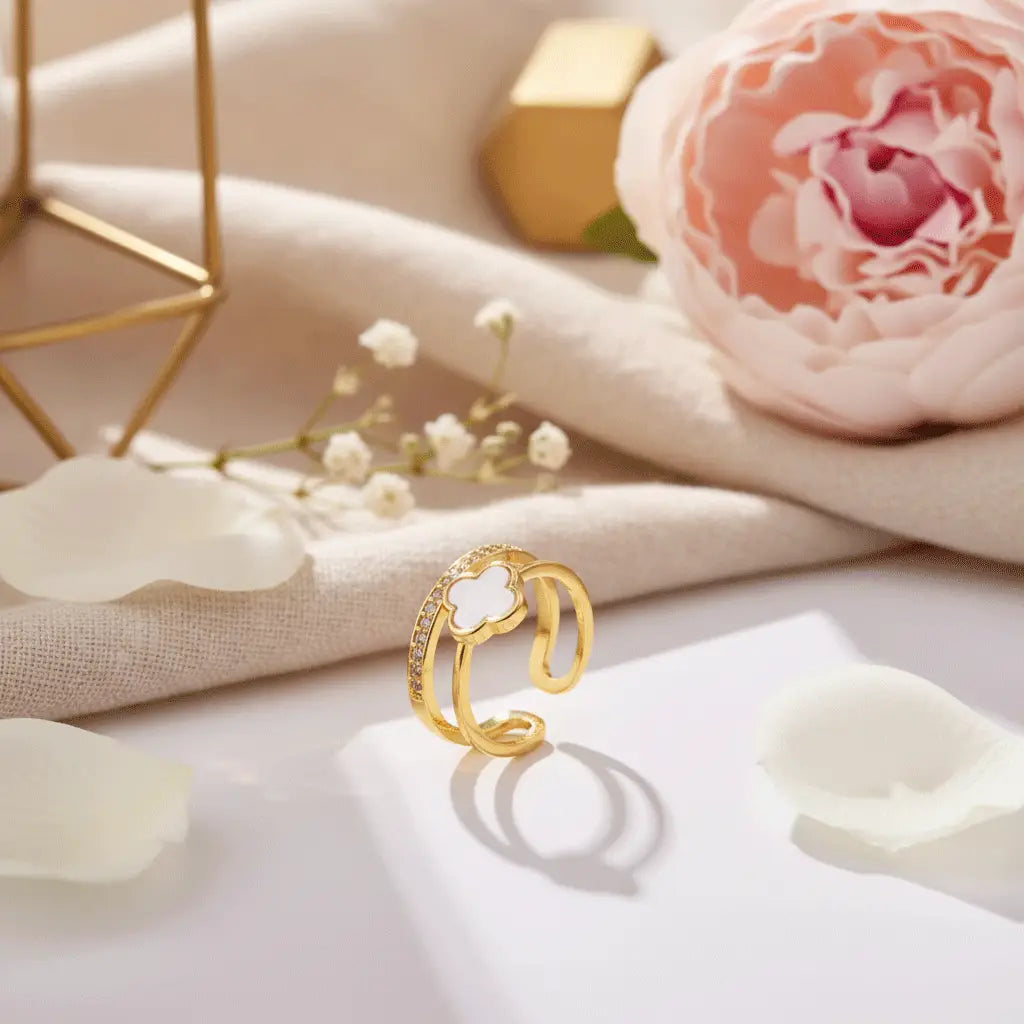 White Clover Ring with gold dual-band design and crystal accents displayed with soft petals and floral decor.